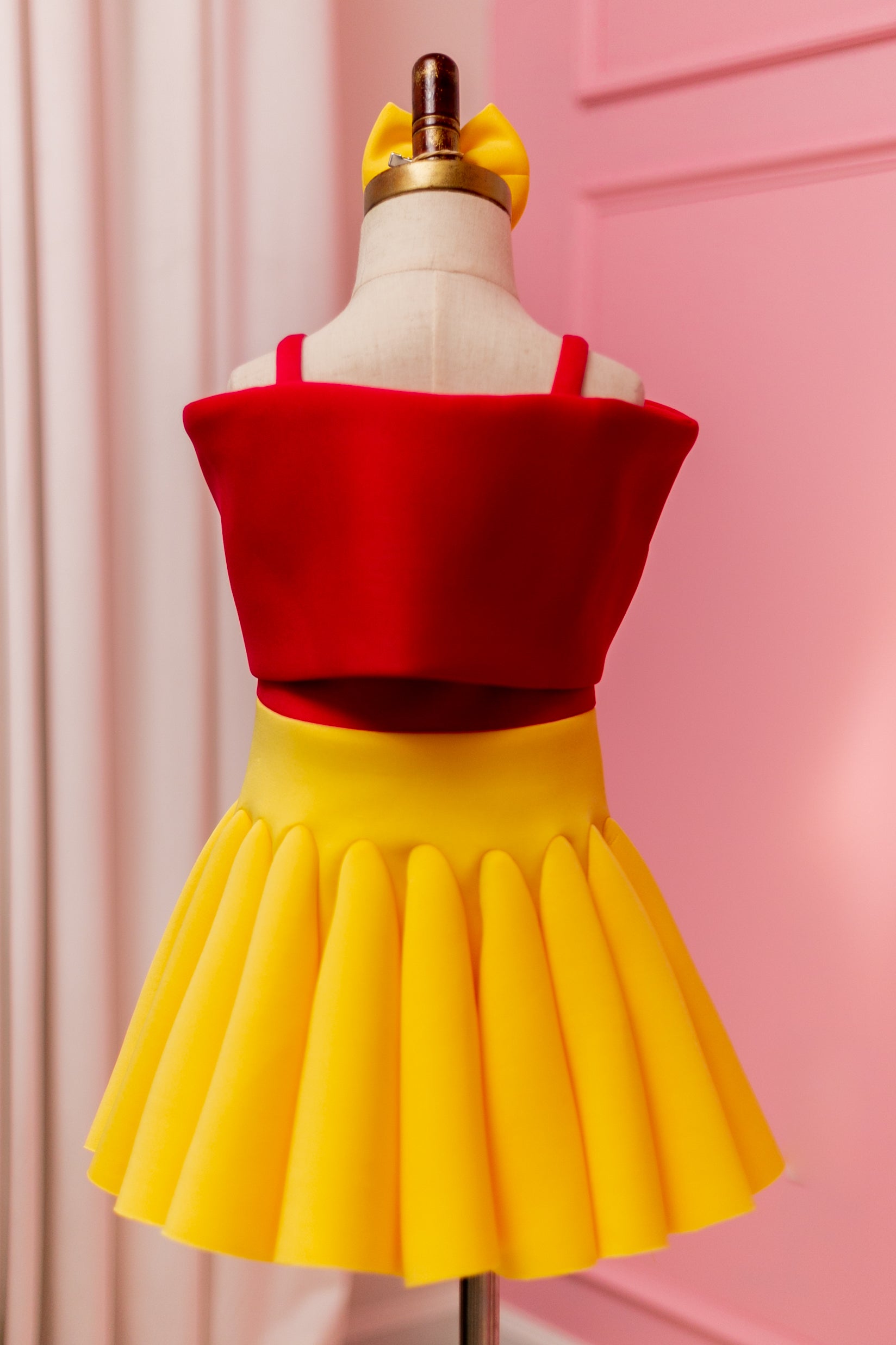 Backview of Fuchsia pink and yellow big bow dress displayed on design stand