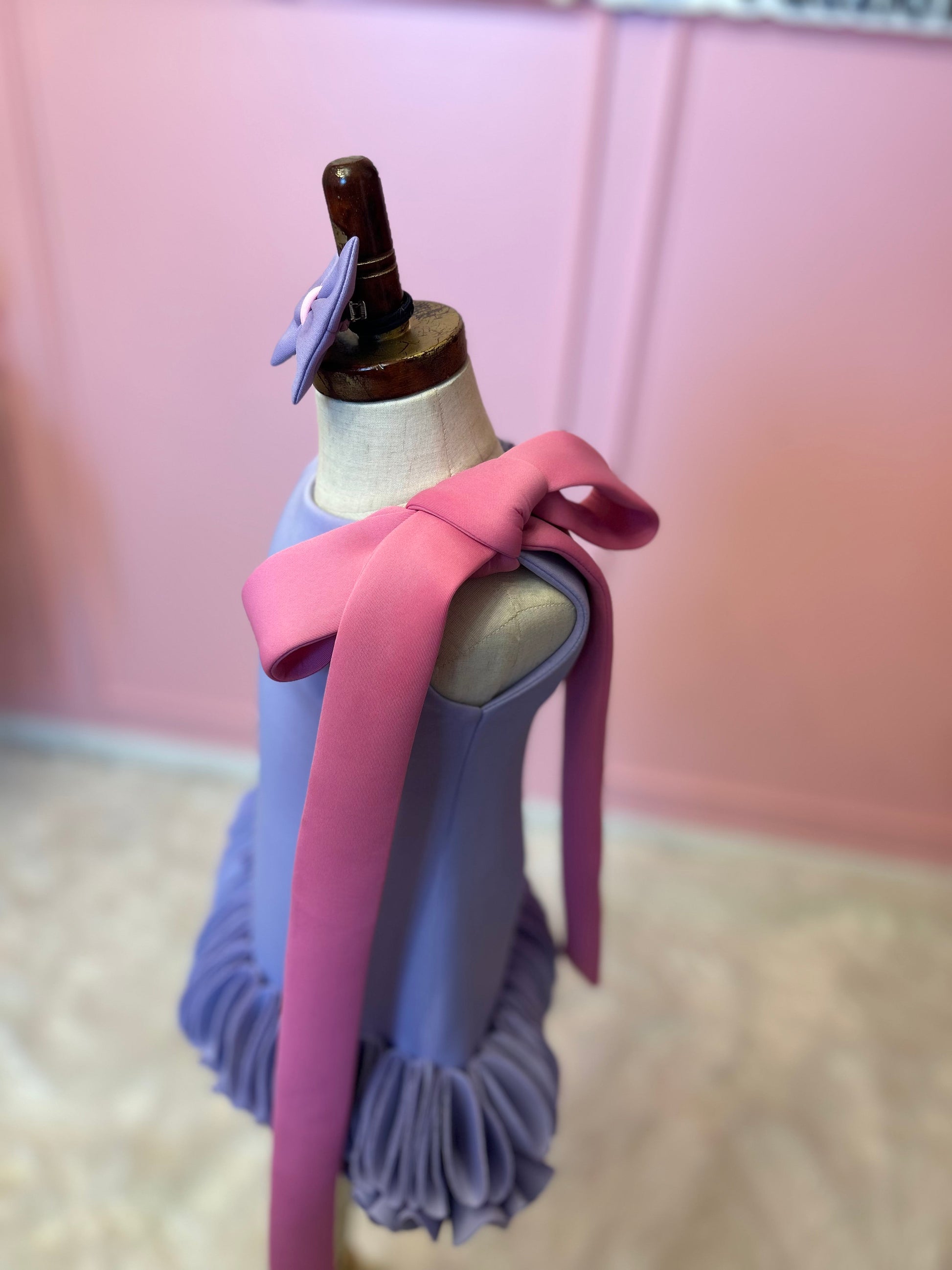 side view of Blue sleeveless straight cut floral dress for kids displayed on a fashion stand, showing pink bow