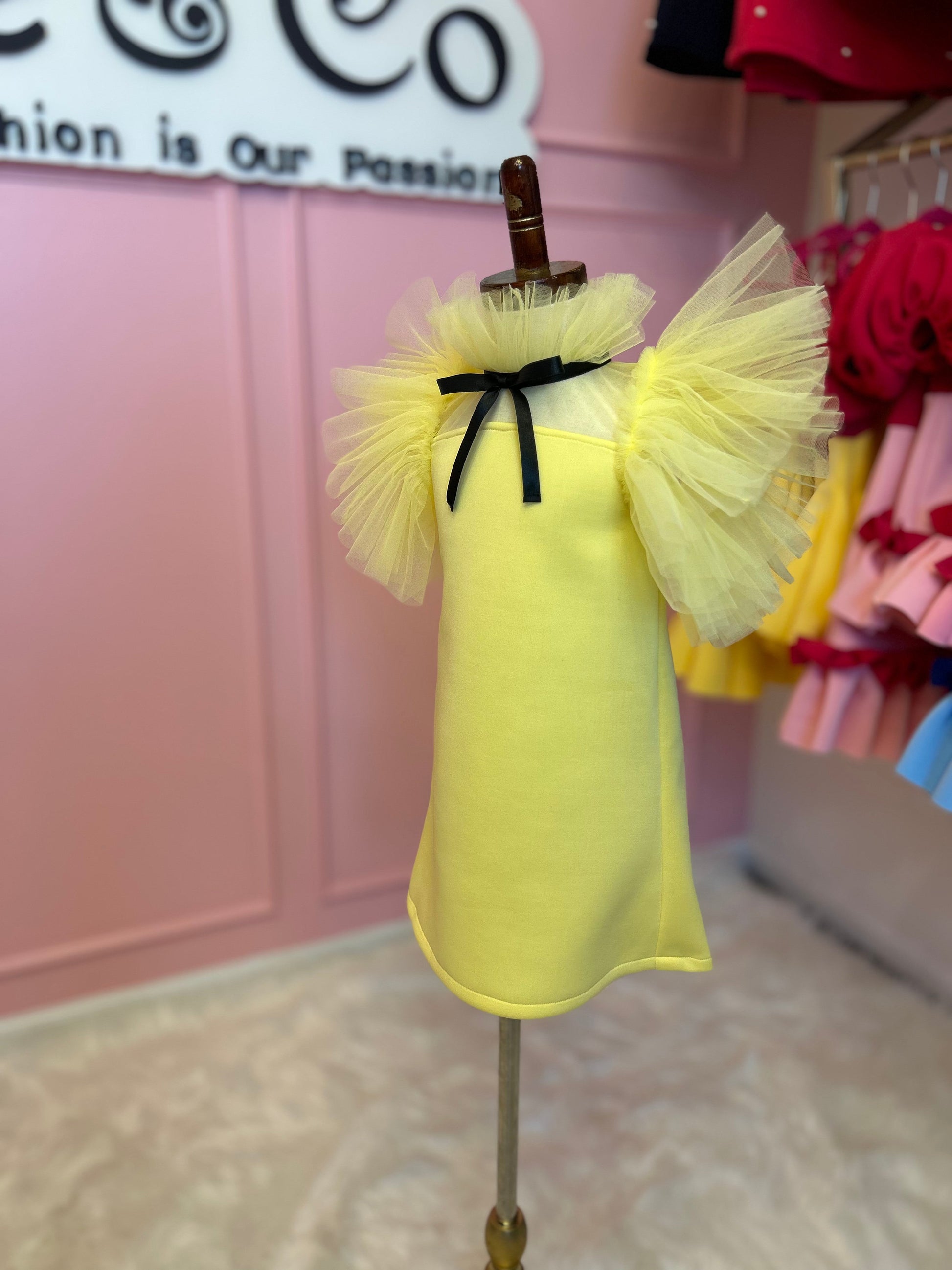 Side view Lemon yellow dress with tulle fluttering around the neck and sleeves, displayed on a fashion stand