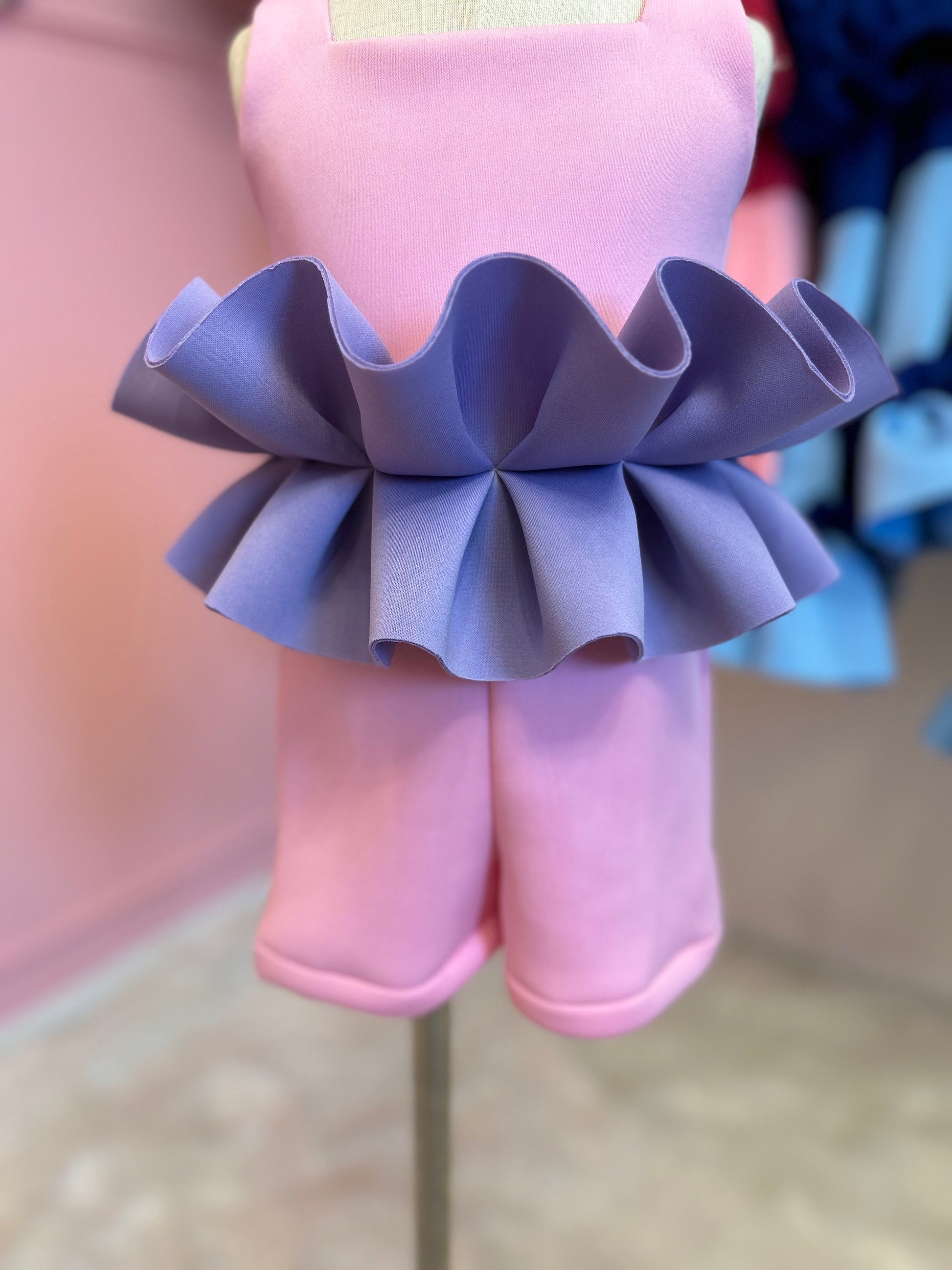 Close up view of Pink romper with purple ruffles displayed on a fashion stand